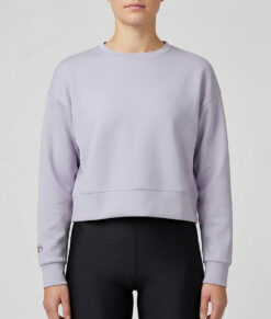 Kvinlig modell visar vår lavendelfärgade magkorta Cloud Crop Sweater framifrån mot en ljusgrå bakgrund.