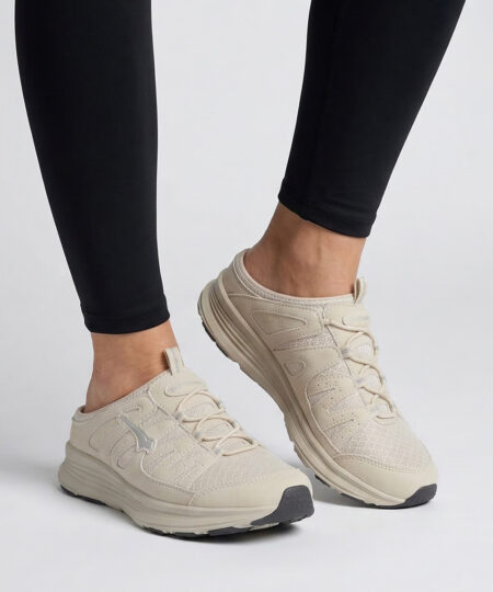 Female model shows off a sand colored bagheera freetime slip-in slipper. The model is standing from the front in a studio with a light gray background. 