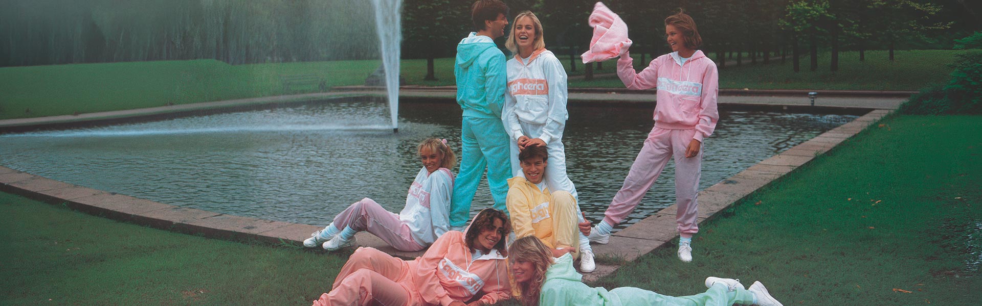 Ett gäng ungdomar ligger i gräset framför en fontän och har på sig Bagheera klassiska 80-tals hoodie Montana i olika pastellfärger.
