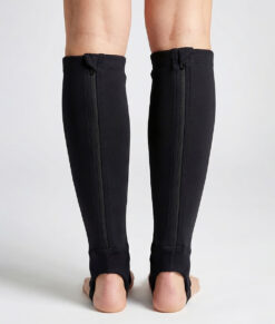 Kvinlig modell visar ett par svarta skenbensskydd i unisexmodell. Modellen står bakifrån i en studio med ljusgrå bakgrund.