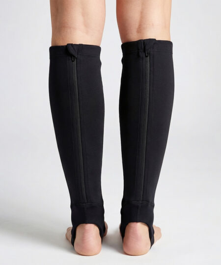 Kvinlig modell visar ett par svarta skenbensskydd i unisexmodell. Modellen står bakifrån i en studio med ljusgrå bakgrund.