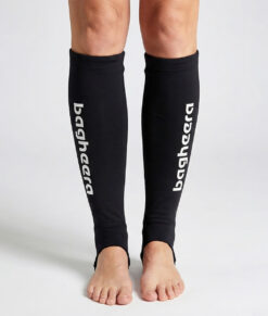 Kvinlig modell visar ett par svarta skenbensskydd i unisexmodell. Modellen står framifrån i en studio med ljusgrå bakgrund.