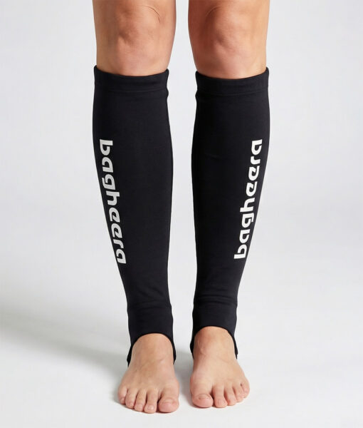 Kvinlig modell visar ett par svarta skenbensskydd i unisexmodell. Modellen står framifrån i en studio med ljusgrå bakgrund.