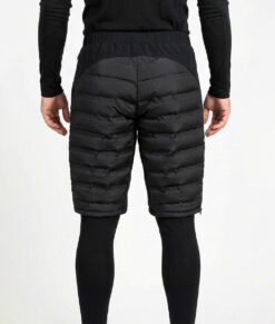 Manlig modell visar ett par svarta vadderade shorts med dragkedja i herrmodell. Modellen har på sig ett svart underställ och står i en studio med ljusgrå bakgrund bakifrån.