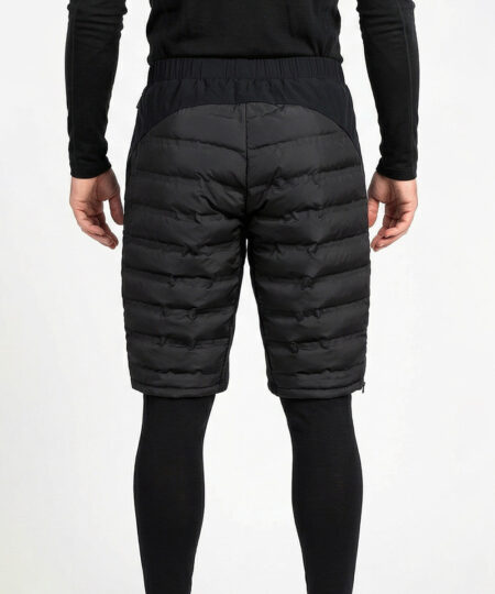 Manlig modell visar ett par svarta vadderade shorts med dragkedja i herrmodell. Modellen har på sig ett svart underställ och står i en studio med ljusgrå bakgrund bakifrån.