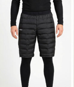 Manlig modell visar ett par svarta vadderade shorts med dragkedja i herrmodell. Modellen har på sig ett svart underställ och står i en studio med ljusgrå bakgrund framifrån.