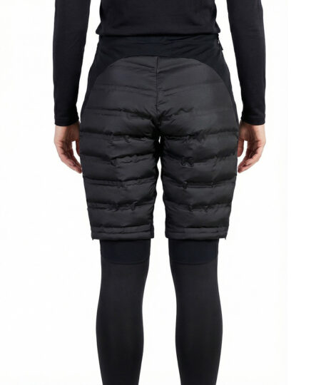 Kvinlig modell visar ett par svarta vadderade shorts med dragkedja i dammodell. Modellen har på sig ett svart underställ och står i en studio med ljusgrå bakgrund bakifrån.