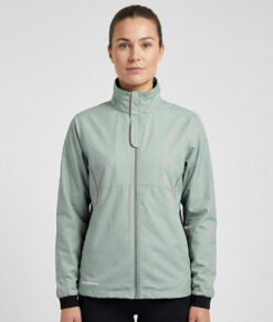 Kvinlig modell visar en ljusgrön vind- och vattentät träningsjacka Selva för dam i en studio med ljusgrå bakgrund. Modellen står framifrån.