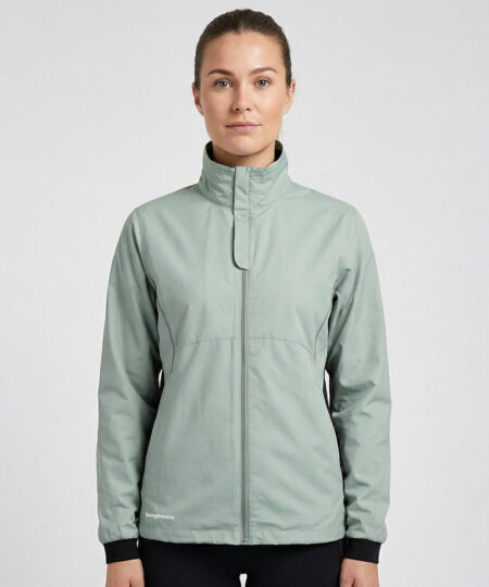 Kvinlig modell visar en ljusgrön vind- och vattentät träningsjacka Selva för dam i en studio med ljusgrå bakgrund. Modellen står framifrån.
