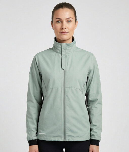 Kvinlig modell visar en ljusgrön vind- och vattentät träningsjacka Selva för dam i en studio med ljusgrå bakgrund. Modellen står framifrån.