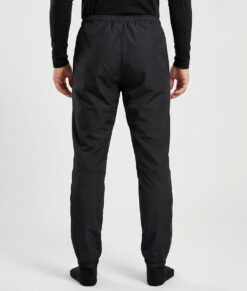 Manlig modell visar ett par svarta vind- och vattentäta träningsbyxor Selva för herr i en studio med ljusgrå bakgrund. Modellen står bakifrån.