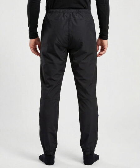 Manlig modell visar ett par svarta vind- och vattentäta träningsbyxor Selva för herr i en studio med ljusgrå bakgrund. Modellen står bakifrån.