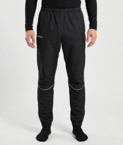 Manlig modell visar ett par svarta vind- och vattentäta träningsbyxor Selva för herr i en studio med ljusgrå bakgrund. Modellen står framifrån.