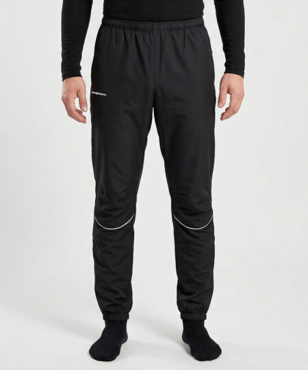 Manlig modell visar ett par svarta vind- och vattentäta träningsbyxor Selva för herr i en studio med ljusgrå bakgrund. Modellen står framifrån.