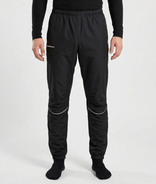 Manlig modell visar ett par svarta vind- och vattentäta träningsbyxor Selva för herr i en studio med ljusgrå bakgrund. Modellen står framifrån.