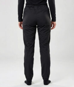 Kvinlig modell visar ett par svarta vind- och vattentäta träningsbyxor Selva för dam i en studio med ljusgrå bakgrund. Modellen står bakifrån.