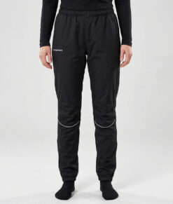 Kvinlig modell visar ett par svarta vind- och vattentäta träningsbyxor Selva för dam i en studio med ljusgrå bakgrund. Modellen står framifrån.