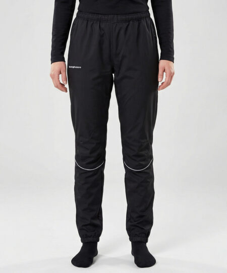 Kvinlig modell visar ett par svarta vind- och vattentäta träningsbyxor Selva för dam i en studio med ljusgrå bakgrund. Modellen står framifrån.