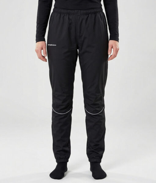 Kvinlig modell visar ett par svarta vind- och vattentäta träningsbyxor Selva för dam i en studio med ljusgrå bakgrund. Modellen står framifrån.