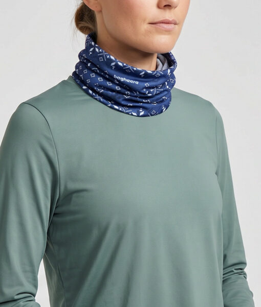 Kvinlig modell visar en blå Dalecarlianmönstrad tube i en studio med ljusgrå bakgrund. Modellen står framifrån.