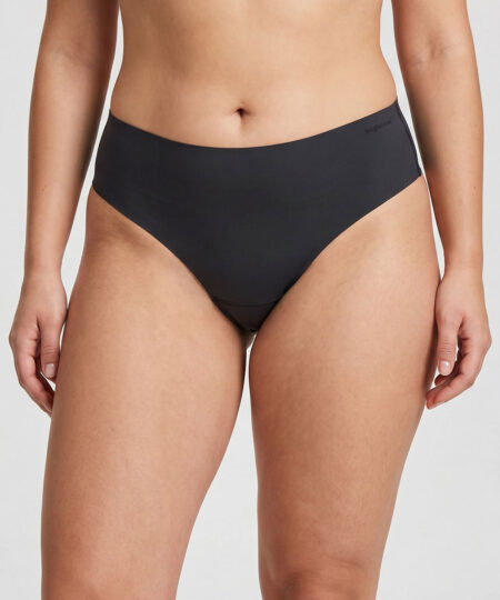 Kvinlig modell visar ett par svarta Swift Thong stringtrosor för dam. Bilden visar modellen framifrån i en studio med ljusgrå bakgrund.