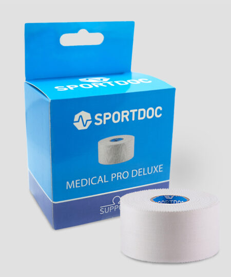 En rulle vit Sportdoc medical pro deluxe sporttape visas framför den tillhörande förpackningen. Tapen visas mot ljusgrå bakgrund.
