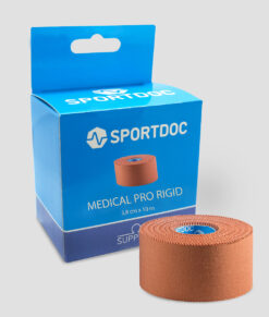 En rulle beige Sportdoc medical pro rigid sporttape visas framför den tillhörande förpackningen. Tapen visas mot ljusgrå bakgrund.