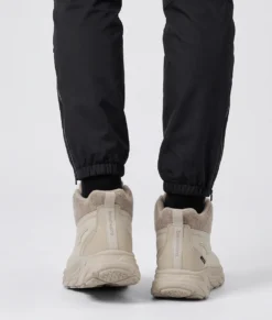 Kvinlig modell visar Grace som är en sandfärgad vattenavvisande varm ankelboot med snabbsnörningssystem. Modellen visar skon bakifrån i en studio med ljusgrå bakrund.
