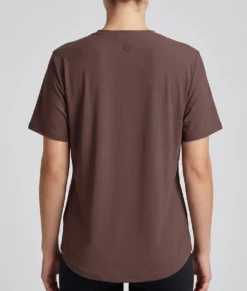 Kvinlig modell visar en brun tränings t-shirt med lite lösare passform. Modellen visar t-shirten bakifrån i en studio med ljusgrå bakgrund.
