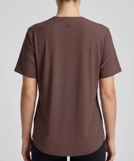 Kvinlig modell visar en brun tränings t-shirt med lite lösare passform. Modellen visar t-shirten bakifrån i en studio med ljusgrå bakgrund.