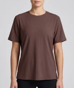 Kvinlig modell visar en brun tränings t-shirt med lite lösare passform. Modellen visar t-shirten framifrån i en studio med ljusgrå bakgrund.