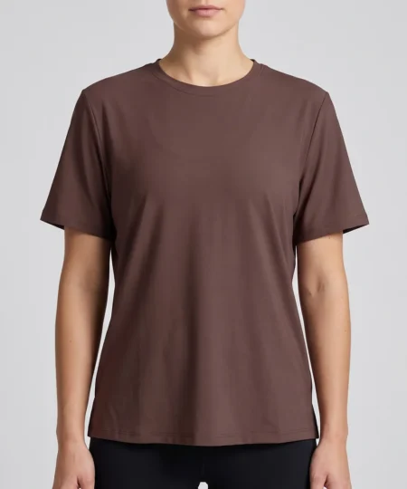 Kvinlig modell visar en brun tränings t-shirt med lite lösare passform. Modellen visar t-shirten framifrån i en studio med ljusgrå bakgrund.