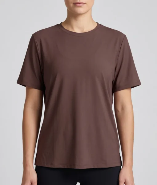 Kvinlig modell visar en brun tränings t-shirt med lite lösare passform. Modellen visar t-shirten framifrån i en studio med ljusgrå bakgrund.