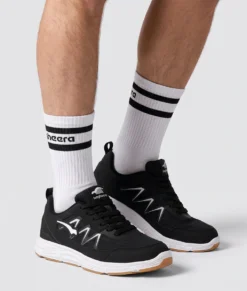 Manlig modell visar Vortex som är en svart inomhussko. Modellen visar skon snett från sidan i en studio med ljusgrå bakrund.