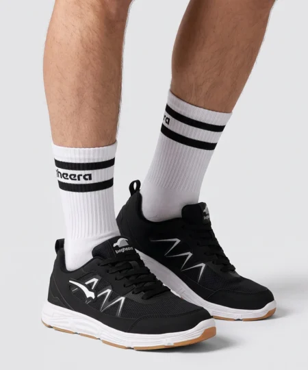 Manlig modell visar Vortex som är en svart inomhussko. Modellen visar skon snett från sidan i en studio med ljusgrå bakrund.