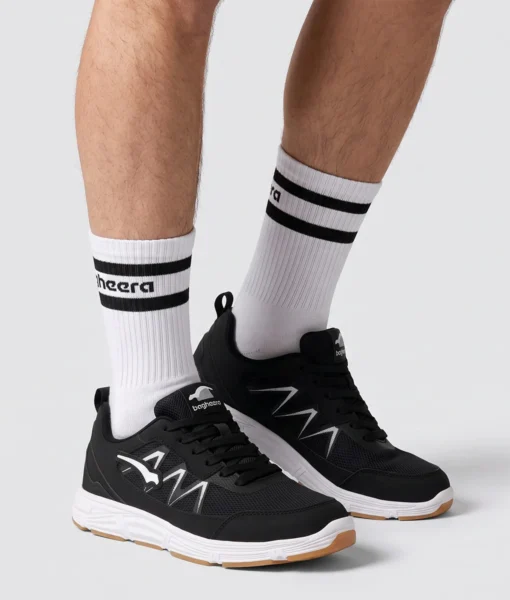 Manlig modell visar Vortex som är en svart inomhussko. Modellen visar skon snett från sidan i en studio med ljusgrå bakrund.