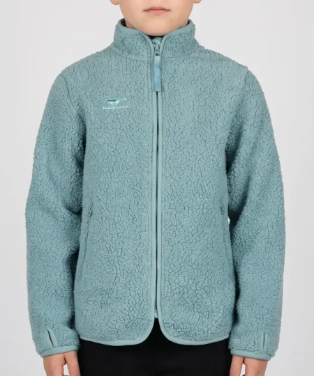 Pojkmodell visar en duvblå Comfy jacket i mjuk pilé. Modellen visar jackan framifrån i en studio med ljusgrå bakgrund.
