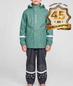 Pojkmodell modell visar en dimblå regnjacka och svarta regnbyxor i ett paketpris. Modellen står framifrån i en studio med ljusgrå bakgrund.