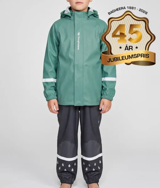 Pojkmodell modell visar en dimblå regnjacka och svarta regnbyxor i ett paketpris. Modellen står framifrån i en studio med ljusgrå bakgrund.