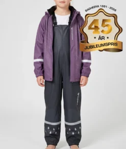 Tjejmodell modell visar en lila regnjacka och svarta regnbyxor i ett paketpris. Modellen står framifrån i en studio med ljusgrå bakgrund.
