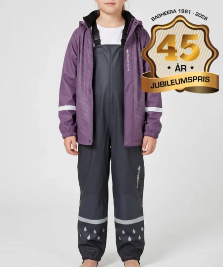 Tjejmodell visar en lila regnjacka och svarta regnbyxor i ett paketpris. Modellen står framifrån i en studio med ljusgrå bakgrund.