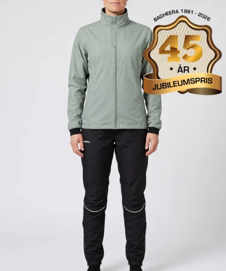 Kvinlig modell visar Selva ljusgrön jacka och svarta byxor i ett paketpris. Modellen står framifrån i en studio med ljusgrå bakgrund.