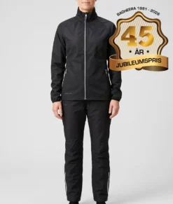 Kvinlig modell visar Selva svart jacka och svarta byxor i ett paketpris. Modellen står framifrån i en studio med ljusgrå bakgrund.